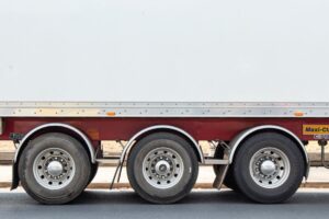 Drei Achsen und Reifen eines Lkw-Anhängers auf Asphalt.