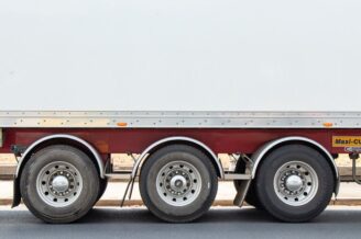 Drei Achsen und Reifen eines Lkw-Anhängers auf Asphalt.