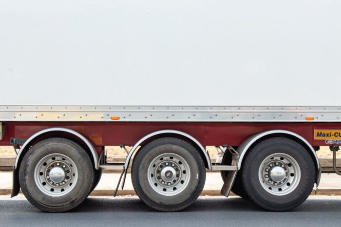 Drei Achsen und Reifen eines Lkw-Anhängers auf Asphalt.