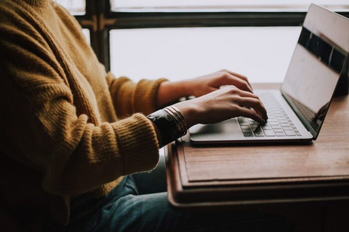 Person arbeitet konzentriert an einem Laptop an einem Holztisch