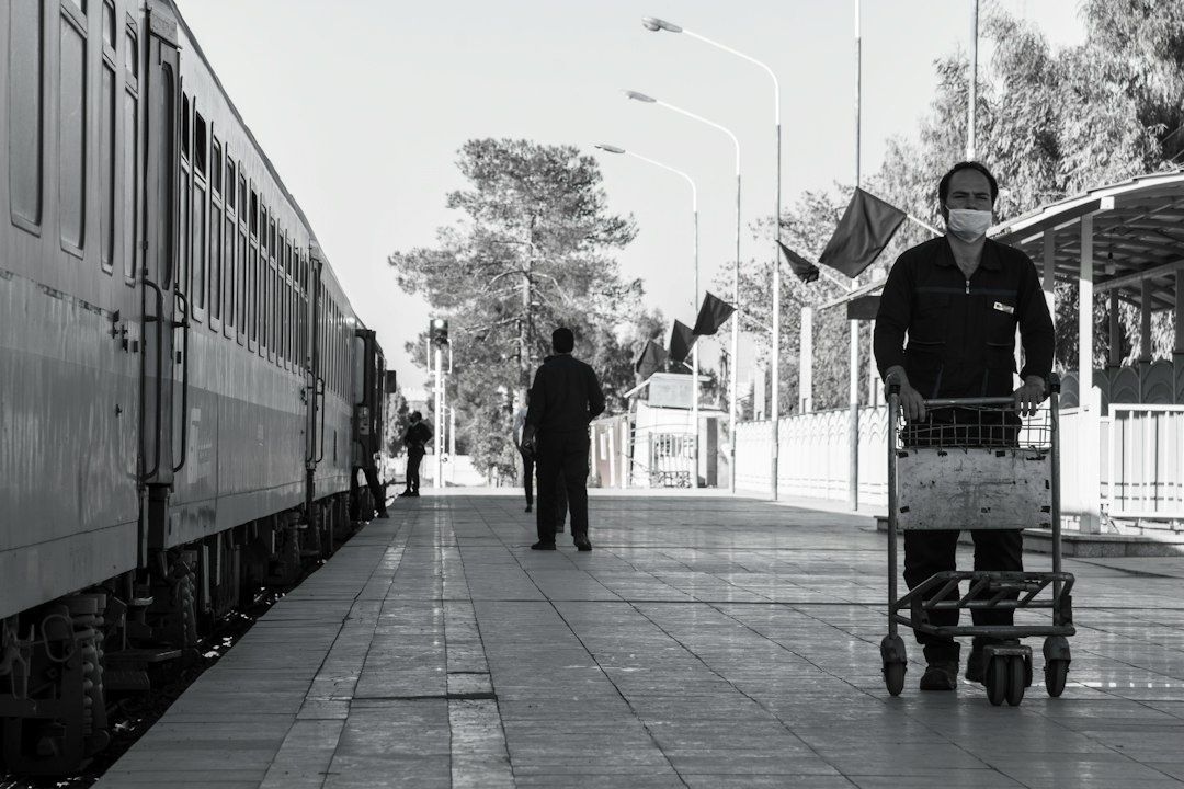 Bahnhof mit Zug, Gepäckwagen und wartenden Reisenden auf dem Bahnsteig