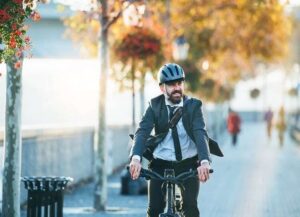 Geschäftsmann mit Helm fährt mit dem Fahrrad durch eine herbstliche Stadtstraße
