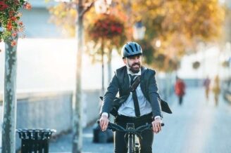 Geschäftsmann mit Helm fährt mit dem Fahrrad durch eine herbstliche Stadtstraße